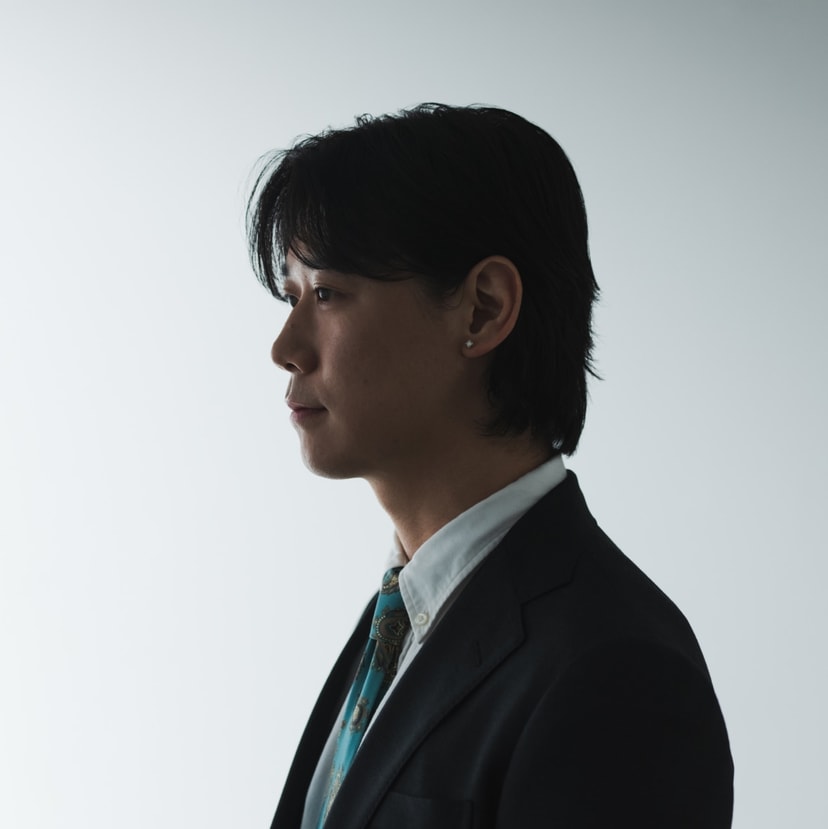 スーツ姿で横を向く小袋成彬の写真